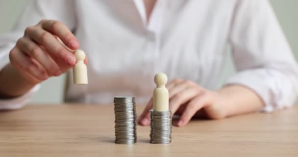 Eine Frau im weißen Hemd legt Holzfiguren auf Türme aus Münzen, die am Schreibtisch sitzen. Konzept des Geldverdienens von Firmenmitgliedern in Zeitlupe - Filmmaterial, Video
