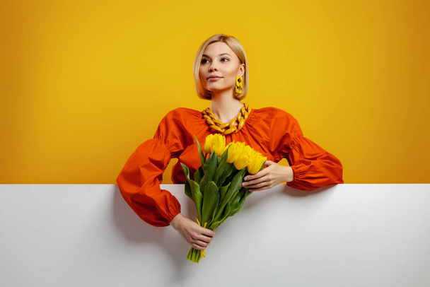 Beautiful young woman holding bunch of tulips against yellow background - Foto, afbeelding