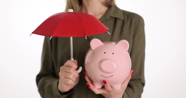 Femme tient tirelire rose sous parapluie rouge comme assurance. Femme enregistre et accumule des finances à l'aide de la boîte à monnaie. Fruit financier - Séquence, vidéo