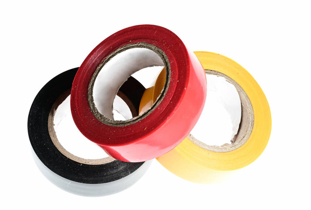 129 / 500Stapel van drie rood-gele zwart veelkleurige duct tape rollen van elektrische tape als een concept voor elektrisch contact isoleren op witte achtergrond - Foto, afbeelding