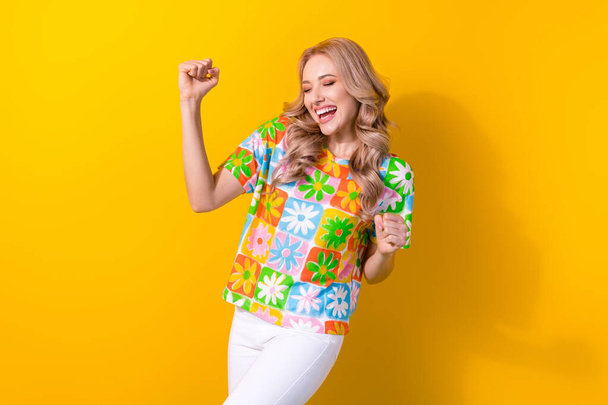 Photo of dreamy lucky lady wear flower print t-shirt closed eyes rising fists isolated yellow color background. - Foto, Bild
