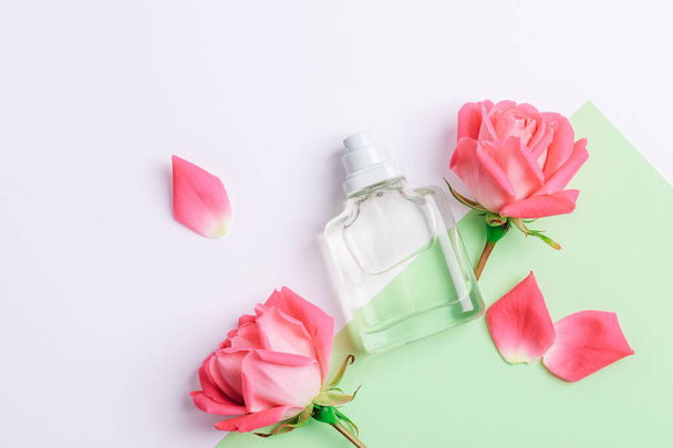 Glass perfume bottle and pink rose flowers on white and green background. Top view, flat lay, mockup. - Fotografie, Obrázek