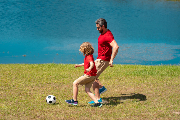 Dad and son playing football together on green meadow. Father and son having fun on football pitch. Dad with kid are having fun and playing football on grass outdoor. Friendly family. Fathers day - Valokuva, kuva