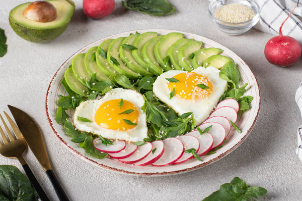 Υγιεινό ρομαντικό πρωινό - τηγανητά αυγά σε σχήμα καρδιάς σερβιρισμένα με αβοκάντο και ραπανάκι, Closeup - Φωτογραφία, εικόνα