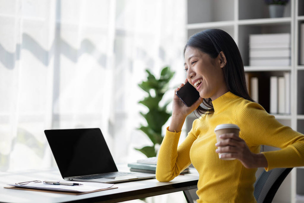 A young woman is a start-up businesswoman, she is talking on the phone, manages and runs her business from a young generation. Startup business management concept. - Photo, image