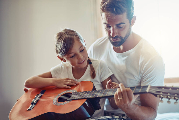 Πατέρας με κόρη, κιθάρα με διδασκαλία και μάθηση στο σπίτι, δέσιμο με αγάπη και δημιουργικότητα. Οικογένεια, άνδρας και κορίτσι μαθαίνουν να παίζουν μουσικό όργανο, μάθημα και μουσική εκπαίδευση με ταλέντο. - Φωτογραφία, εικόνα
