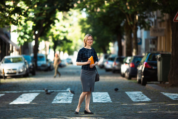 A woman with a notebook in her hands stands on the street. - Foto, afbeelding