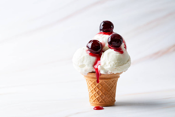 Vanilla ice cream scoop in a serve waffle cone with canned cherries and cherry syrup on a white background, copy space. - Photo, Image