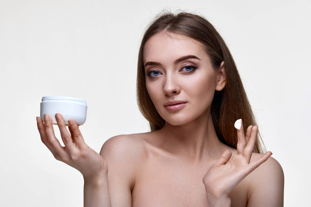 beautiful smiling young woman applying skin care cream on her face on white background - Photo, image