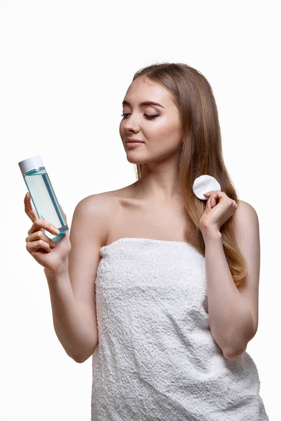 beautiful woman holding bottle with tonic, cleaning skin with cotton pad. Beauty and skin care concept - 写真・画像
