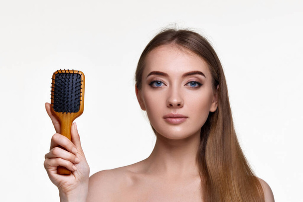 Beautiful brunette woman showing wooden brush and recommend haircare product for healthy long hair isolated on white background - Zdjęcie, obraz