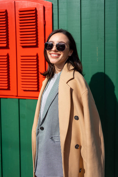 Happy caucasian girl walking Christmas holiday winter day in European city. Brunette woman wears stylish jacket, coat and sunglasses. Positive emotions lifestyle concept - Fotografie, Obrázek
