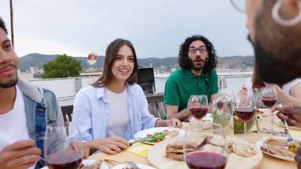 Boldog változatos baráti társaság élvezi vacsora barbecue nyáron otthon terasz. Két fiatal éljenzett vörösborral a bbq partin. Élelmiszer és családi pillanatok koncepció - Felvétel, videó