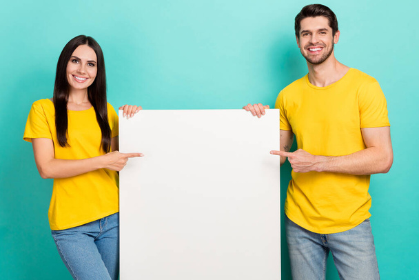 Photo of cheerful positive husband wife dressed yellow t-shirts pointing poster empty space isolated turquoise color background. - Фото, зображення