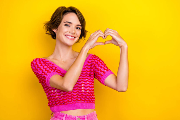 Photo of toothy beaming positive girl dressed off shoulder shirt fingers showing heart symbol isolated on yellow color background. - Fotó, kép