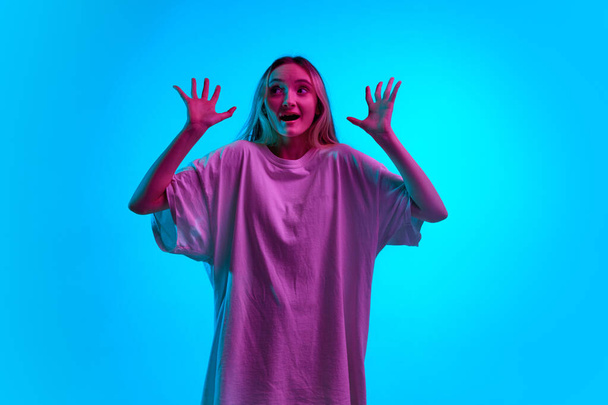 Una persona asustada. Retrato de una joven asustada que sostiene las manos con la boca abierta sobre un fondo de estudio de color azul con luz de neón. Concepto de emociones humanas, estrés, miedo, problemas, fracaso, pérdidas, anuncio - Foto, Imagen