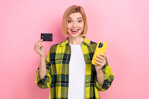 Photo portrait of lovely young lady excited hold credit card telephone ebank wear plaid yellow clothes isolated on pink color background. - Foto, Imagen