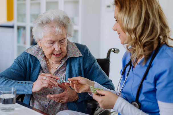 Nurse giving pills to senior woman in her home. - Fotografie, Obrázek