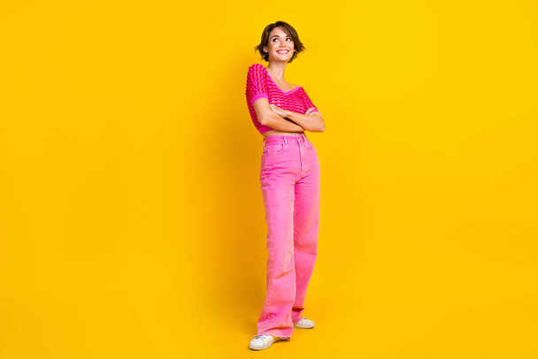 Full size photo of pleasant girl wear knit top pink pants hold arms crossed look at promo empty space isolated on yellow color background. - Zdjęcie, obraz