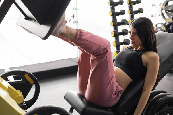 doing strength exercises with a gym machine, fitness training for legs, healthy lifestyle, latin woman with black hair, modern hobbies - Fotoğraf, Görsel
