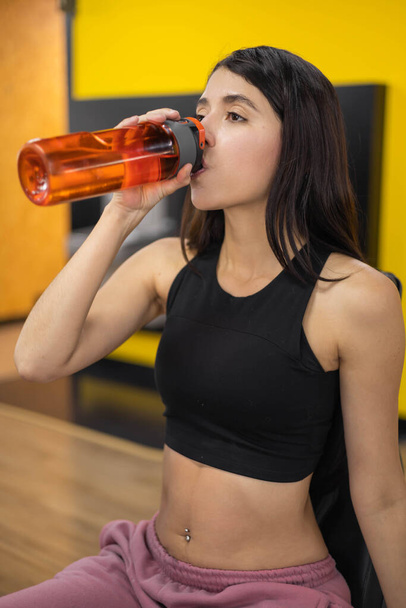 portrait of female model hydrating after workout in gym, young latin woman with long hair wears sportswear, athlete lifestyle - Zdjęcie, obraz
