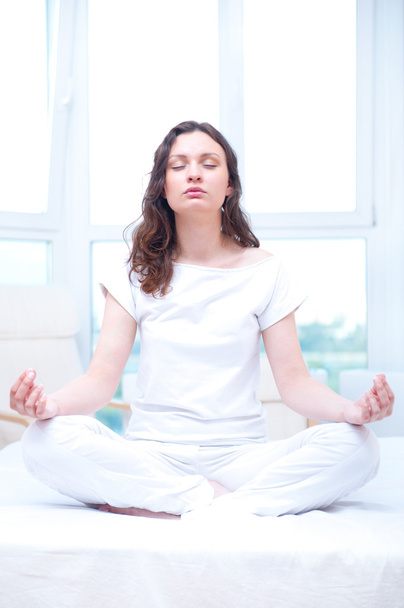 Young woman meditating with closed eyes in bright bedroom sittin - Foto, afbeelding