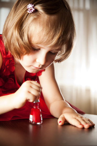 Little girl in a red dress painted nails with nail polish - Foto, afbeelding
