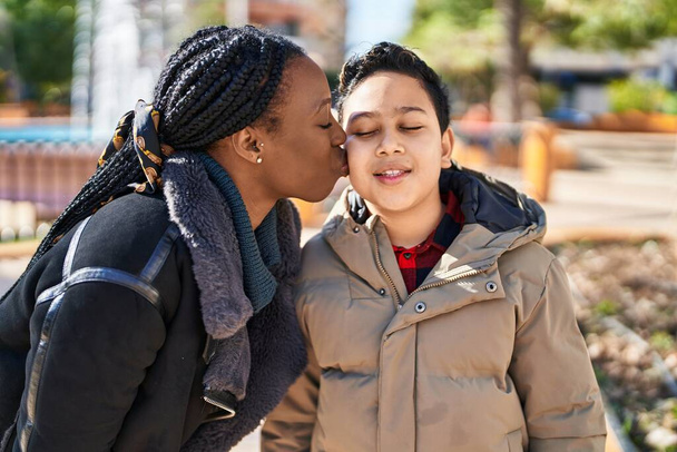 Αφρο-αμερικάνα μητέρα και γιος χαμογελούν με αυτοπεποίθηση και φιλιούνται στο πάρκο - Φωτογραφία, εικόνα