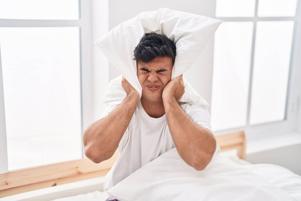 Young hispanic man covering ears for noise at bedroom - Photo, Image