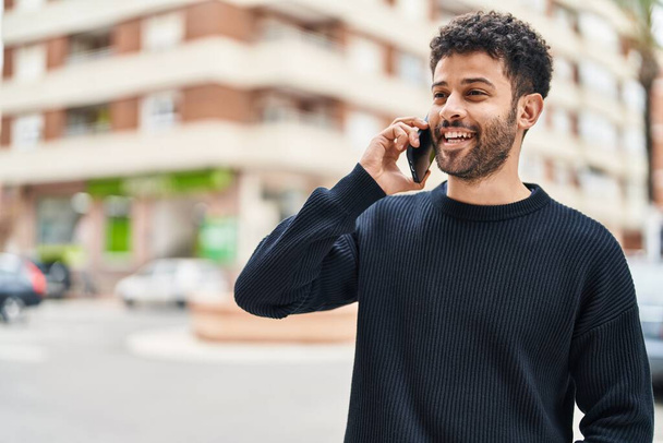 Giovane arabo uomo sorridente fiducioso parlando sullo smartphone in strada - Foto, immagini