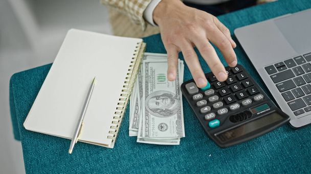 Молодой латиноамериканец считает доллары с помощью калькулятора и пишет заметки в столовой. - Фото, изображение