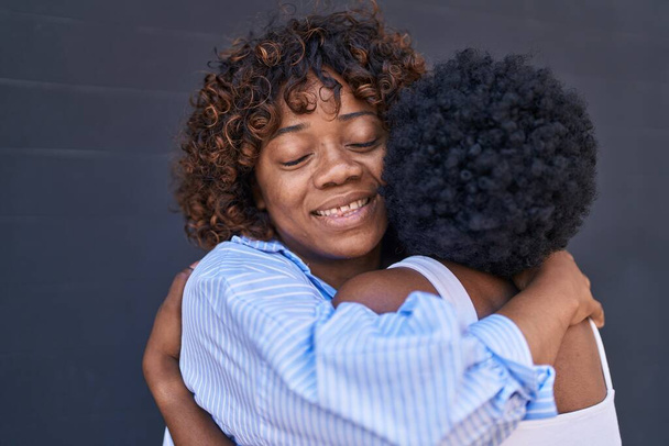 Afroamerikanerinnen Mutter und Tochter umarmen sich vor isoliertem schwarzen Hintergrund - Foto, Bild