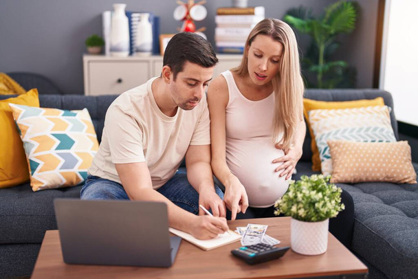 Άνδρας και γυναίκα ζευγάρι αναμένουν μωρό εγγράφως στο σημειωματάριο λογιστική στο σπίτι - Φωτογραφία, εικόνα
