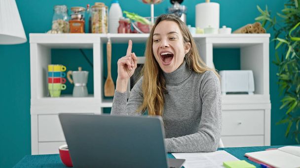 Mujer caucásica joven usando el ordenador portátil con la expresión de la idea en el comedor - Foto, Imagen