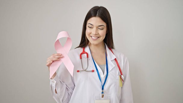 Giovane bella donna ispanica medico sorridente fiducioso tenendo il nastro rosa su isolato sfondo bianco - Foto, immagini