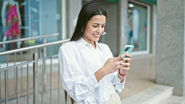 Młoda piękna latynoska kobieta za pomocą smartfona uśmiechnięta na ulicy - Zdjęcie, obraz