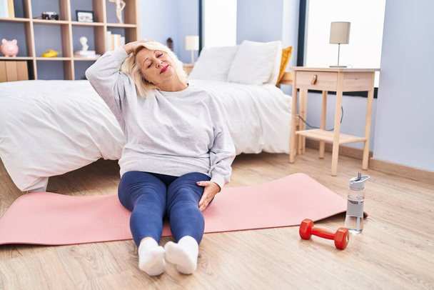 Middle age blonde woman smiling confident stretching at bedroom - Photo, Image