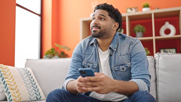 Uomo afroamericano che utilizza smartphone seduto sul divano a casa - Foto, immagini