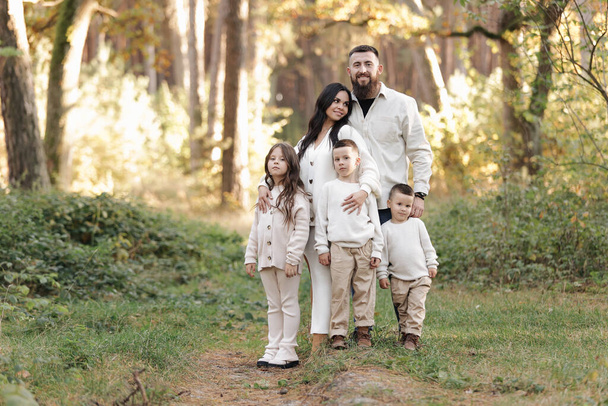 Portrait of big family outdoors. Young Stylish bearded dad with little son on shoulder, beautiful brunette mom, child boy and daughter in autumn park, smiling and looking at camera. Happy family day. - Zdjęcie, obraz