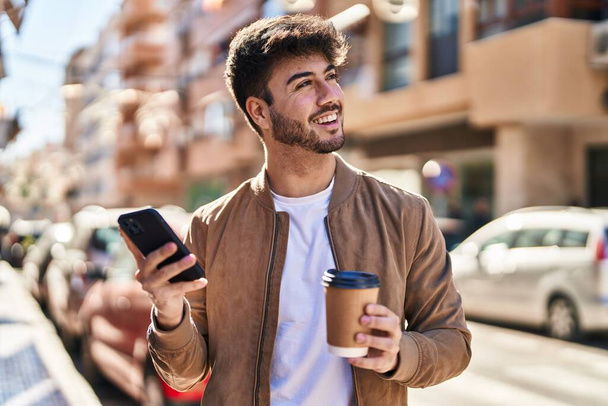 Joven hispano usando smartphone bebiendo café en la calle - Foto, imagen