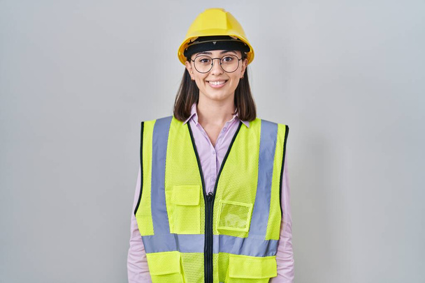 Hispanic girl wearing builder uniform and hardhat with a happy and cool smile on face. lucky person.  - Фото, изображение
