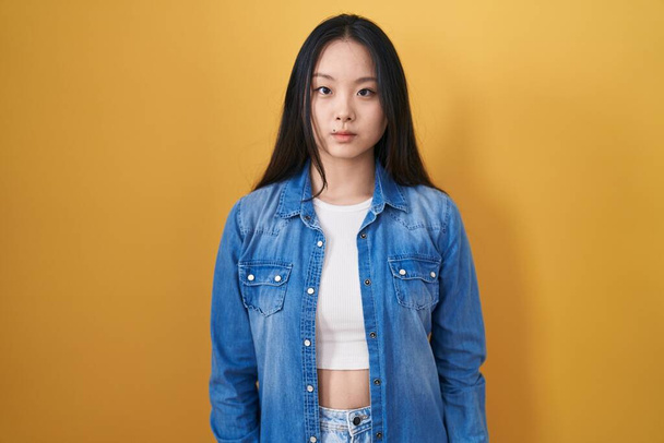 Giovane donna asiatica in piedi su sfondo giallo rilassato con grave espressione sul viso. semplice e naturale guardando la fotocamera.  - Foto, immagini