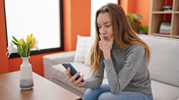 Молода біла жінка використовує смартфон з серйозним виразом вдома
 - Фото, зображення