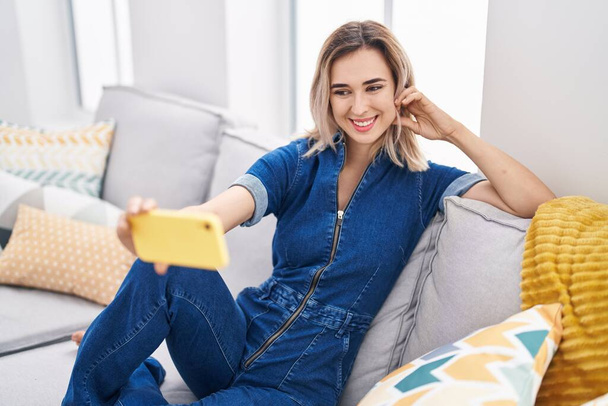 Mladá žena dělat selfie podle smartphone sedí na pohovce doma - Fotografie, Obrázek