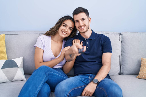Молодая испаноязычная пара смотрит кино, сидя дома на диване - Фото, изображение