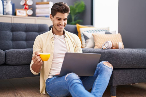 Young hispanic man using laptop drinking coffee at home - Фото, изображение