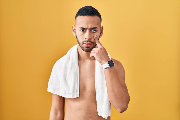 Young hispanic man standing shirtless with towel pointing to the eye watching you gesture, suspicious expression  - Photo, Image
