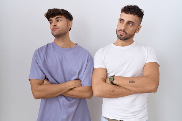 couple gay homosexuel debout sur fond blanc regardant sur le côté avec les bras croisés convaincu et confiant  - Photo, image