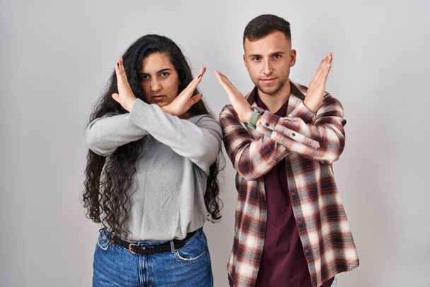 Молода пара іспаномовних, що стоять над виразом відторгнення білого фону, перетинає руки, роблячи негативний знак, розлючене обличчя
  - Фото, зображення