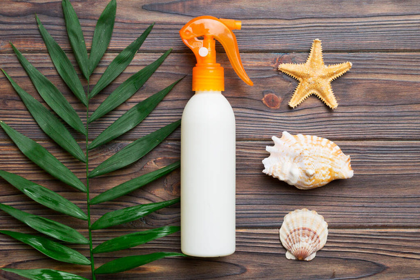 Sunscreen spray bottle. Bottle with sun protection cream and sea shells with tropical green leaf on color background, top view. - Zdjęcie, obraz